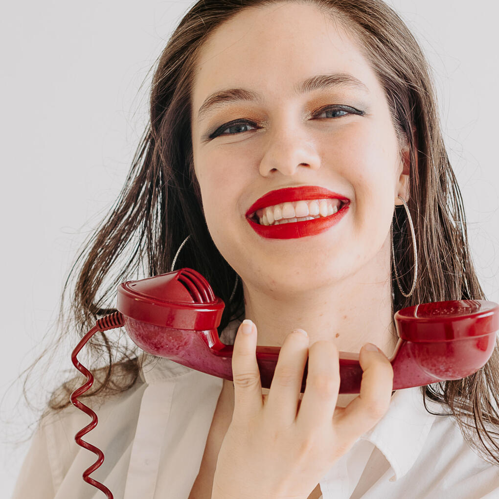 A headshot of Miss Brents against a light background wearing red lipstick smiling directly at the viewer.
